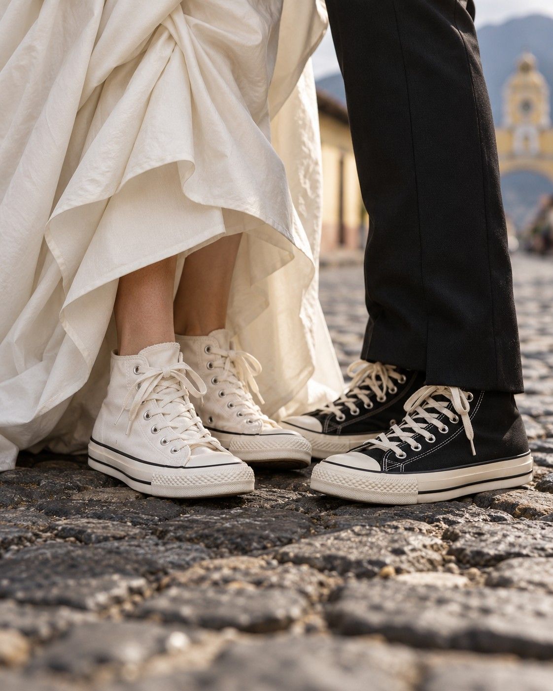 A bride and groom in white and black sneakers on a cobblestone street in Antigua Guatemala, with the Santa Catalina Arch behind them.